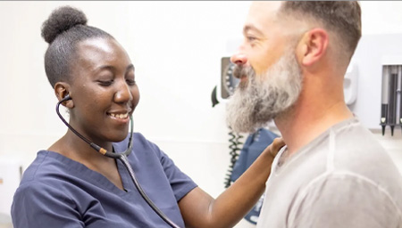 Student in blue scrubs places stethoscope on patient's chest