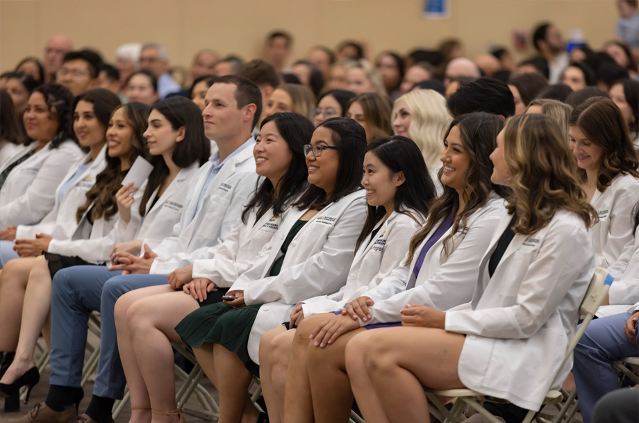 PA students wearing white coats sit side-by-side during an event