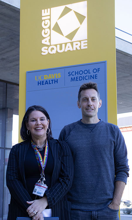 Two adults stand in front of an Aggie Square sign. 