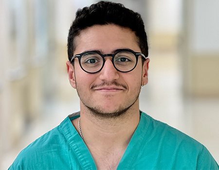 Portrait of a medical student with dark hair, eyeglasses and wearing green scrub v-neck shirt