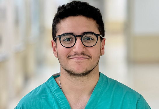 Portrait of a medical student with dark hair, eyeglasses and wearing green scrub v-neck shirt