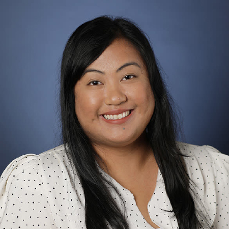 Portrait of a smiling woman with dark, long hair, wearing white shirt with black dots