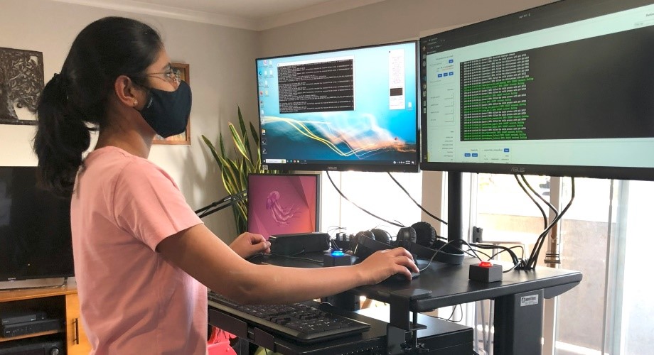 A woman stands in front of two computer monitors