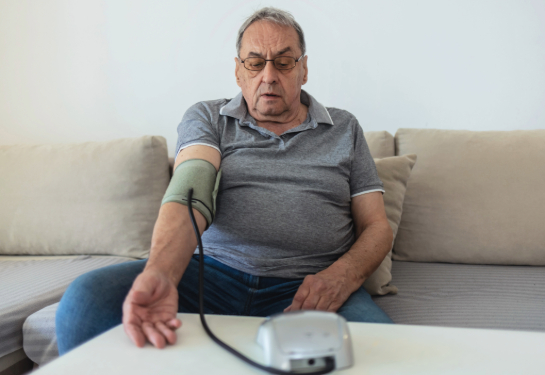 Older man sitting on a couch in a living room measuring his blood pressure 