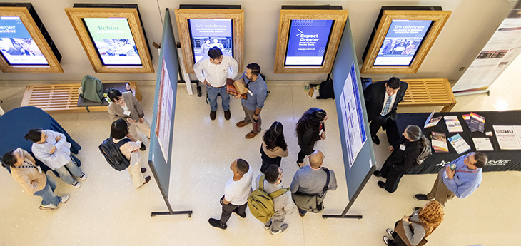 Overhead photo of people viewing poster presentations in sections marked by partitions