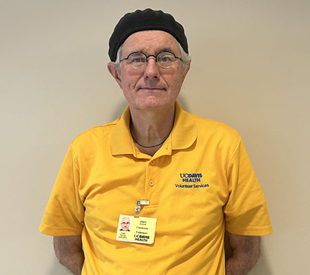 A man wearing a bright yellow shirt and black hat stands for a photo.