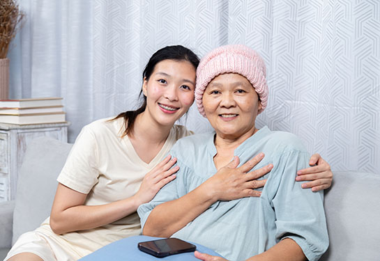 An Asian woman wearing a head scarf due to cancer and her daughter sit in a bed