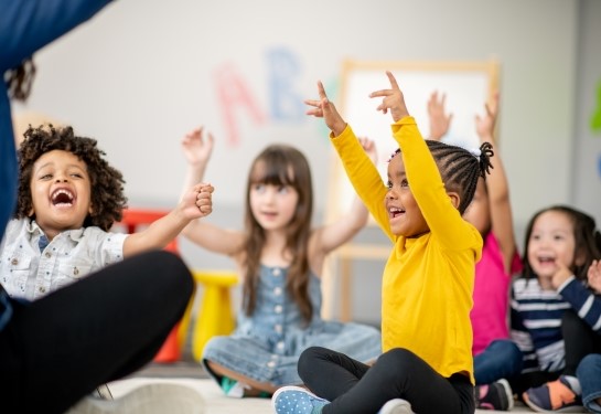 A group of children sit on the floor during a fun activity.