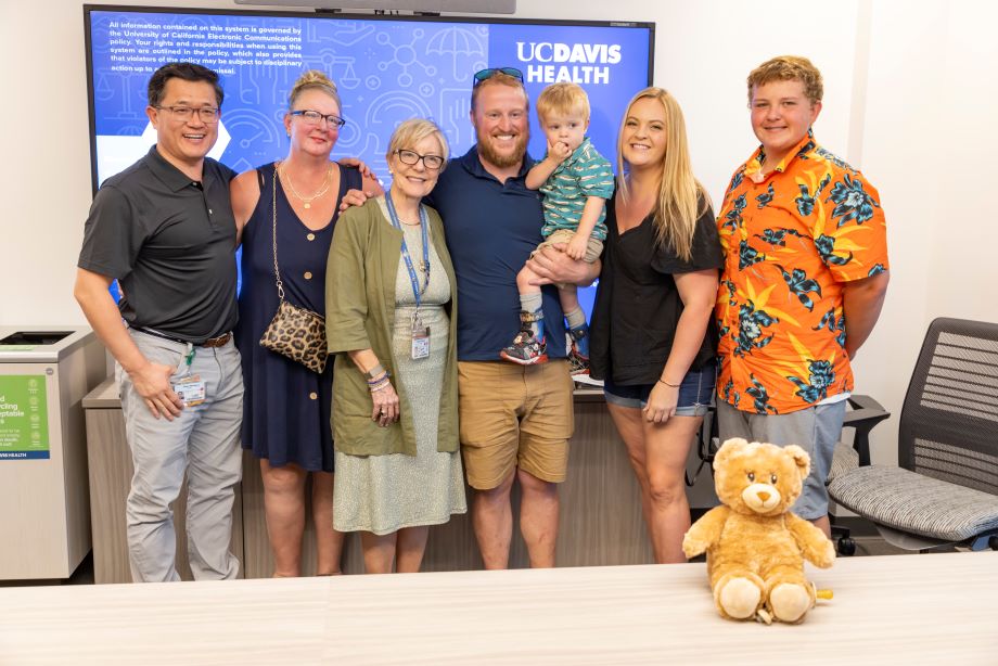 Fetal surgeon Diana Farmer and biomedical engineer Aijun Wang are standing next to the family of a child who participated in the Cure trial. There is a small teddy bear at the right corner of the picture.