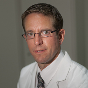 Man with light brown hair and suit smiling into camera.