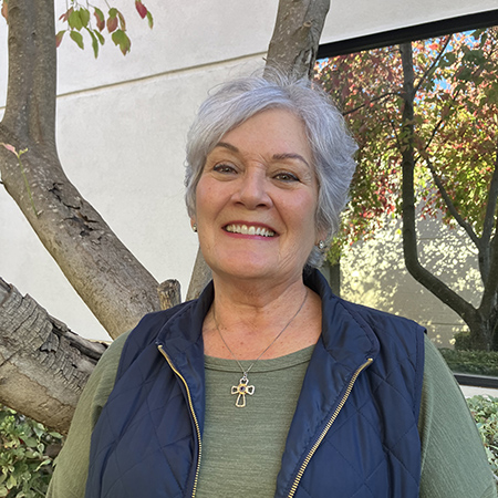 Woman with grey hair, wearing vest in front of exterior of building.