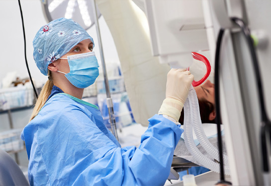 nurse wearing scrubs and surgical hat adjusts equipment in operating room