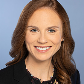 A headshot of a smiling woman with auburn hair.