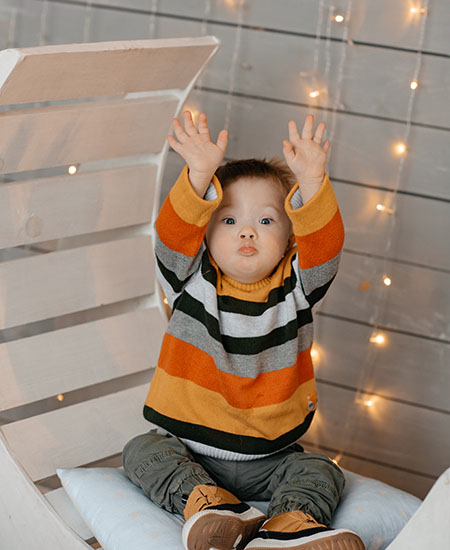 A young boy sits with his hands stretched over his head. 