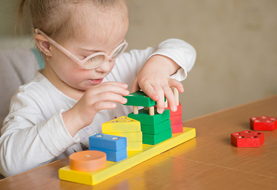A young girl with Down syndrome plays with colorful toys at a table. 