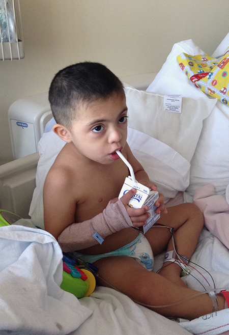Toddler in a hospital bed sipping on a juice box.