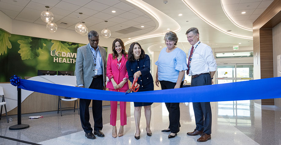 adults stand with a large pair of scissors to cut a ribbon in a health care facility