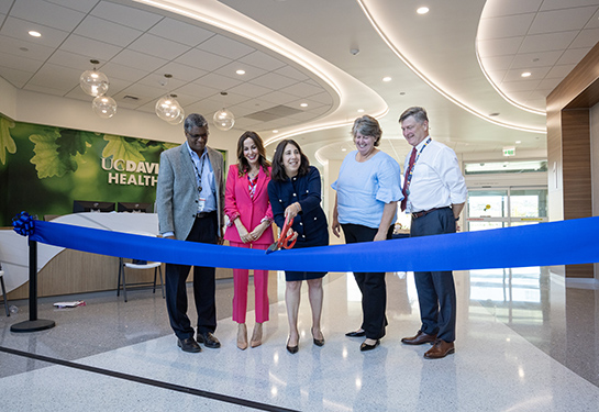 Adults stand together to cut a long blue ribbon at the new Folsom Medical Care Clinic