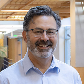 A man with brownish gray hair, wearing a light blue button-down shirt, stands inside a medical building at UC Davis Health.