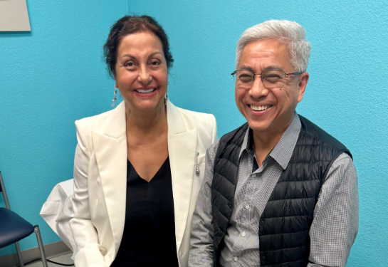 Gita Fulwiler and Frank Ing sitting on patient bed together in clinic.