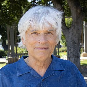 An man with whitish hair, wearing a blue shirt smiles for a portrait.
