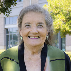 A woman with whitish gray hair and a green and black outfit smiles for a portrait.