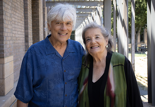 An older man and woman with whitish-gray hair stand in the courtyard of a sandstone building.  