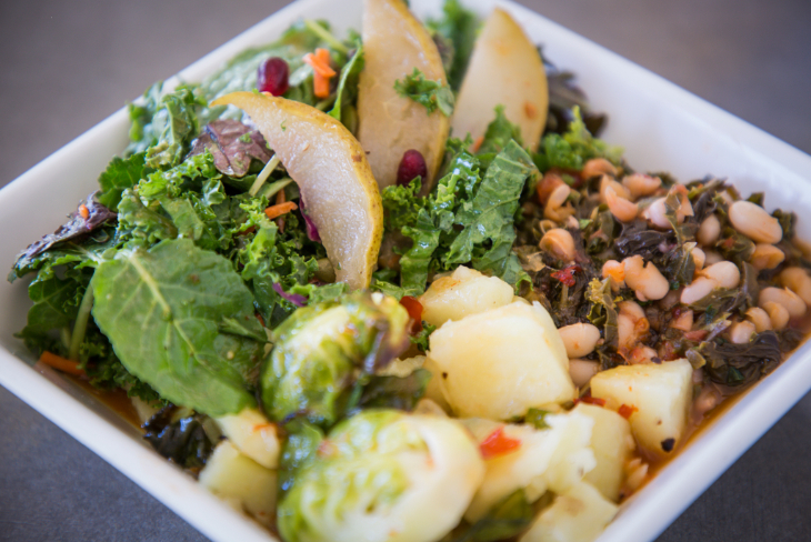 A plate of healthy food, including salad with pear slices, beans with greens and brussels sprouts.