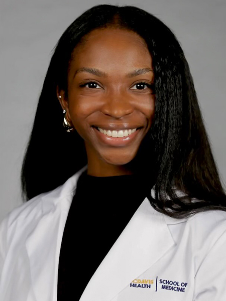 Vertical headshot of a young woman with black hair well past her shoulders smiling, wearing a &ldquo;School of Medicine&rdquo; white lab coat