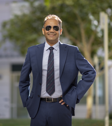 A man stands outside wearing sunglasses and a blue suit.