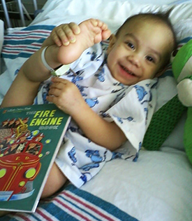 Smiling baby lying in a hospital bed holding foot.