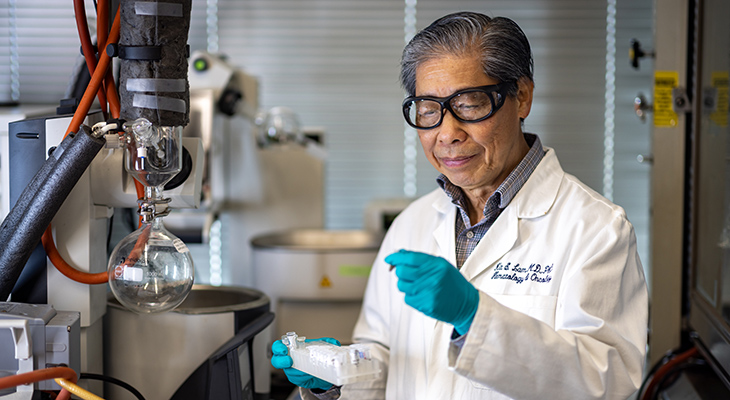 Man in white coat working in a lab, examining a vial.