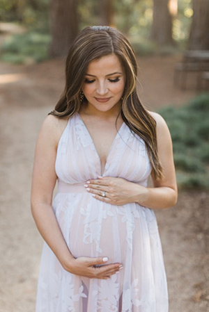 Woman in white dress looking down as she holds pregnant belly.