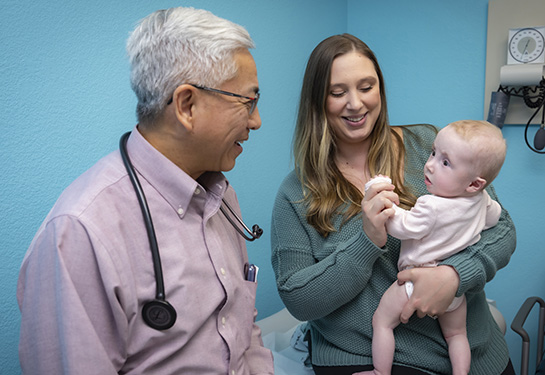 Woman holds baby and man smiles at baby.