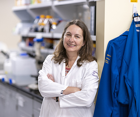 Woman with brown hair and white lab coat smiling into camera with lab in background.