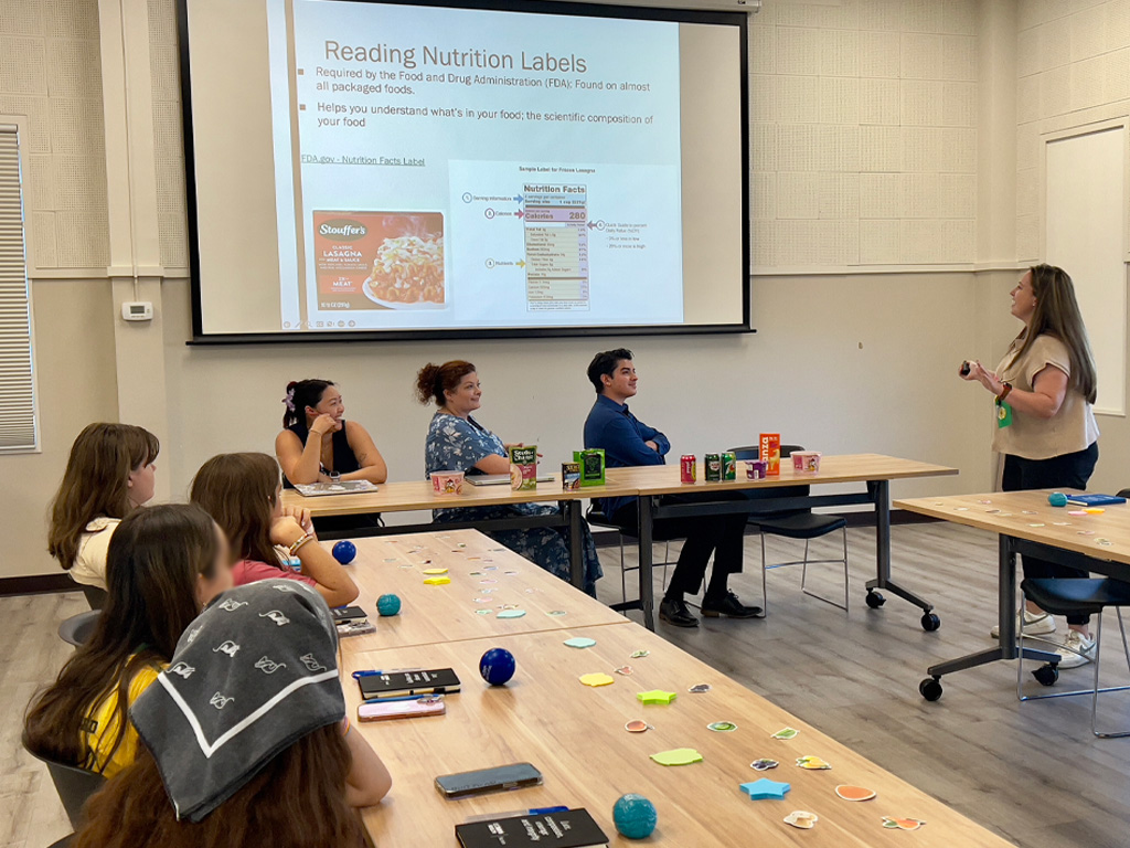 Nursing student in a classroom setting uses a projection screen to teach fellow students how to read nutrition labels.