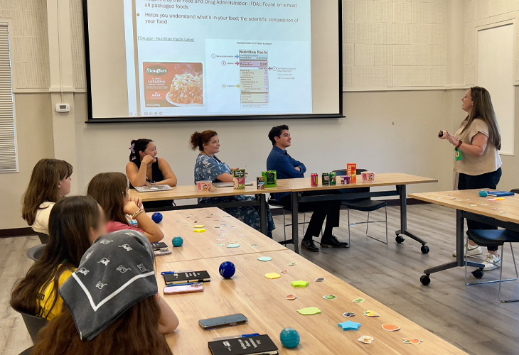 Nursing student in a classroom setting uses a projection screen to teach fellow students how to read nutrition labels.