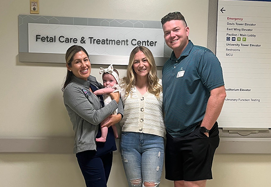 Two women and one man stand in front of the Fetal Care Center sign at UC Davis as one of the women holds an infant.