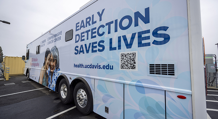 White bus with images of two women and lettering that states &ldquo;Screening Saves Lives&rdquo; and &ldquo;UC Davis Comprehensive Cancer Center&rdquo;