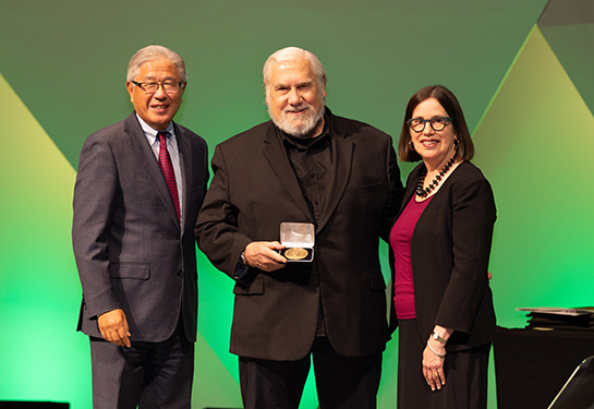 Kenneth W. Kizer is holding a medal in his hand and standing between Victor Dzau and Elena Fuentes-Afflick. 