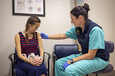 Doctor in green scrubs examines a woman in a red and blue striped top holding a baby