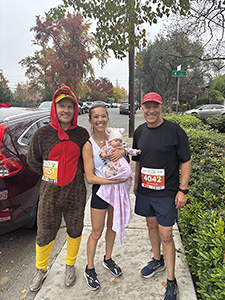 A man in a turkey costume stands next to a woman holding a baby and another man.
