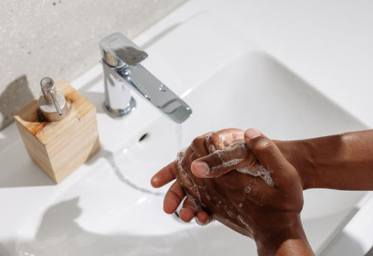 An adult washes their hands in a white sink with hand soap on the counter