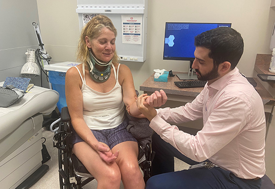 Patti Dailey in a wheelchair, wearing a neck support. Dr. Shane Stone examining the strength in her left hand.