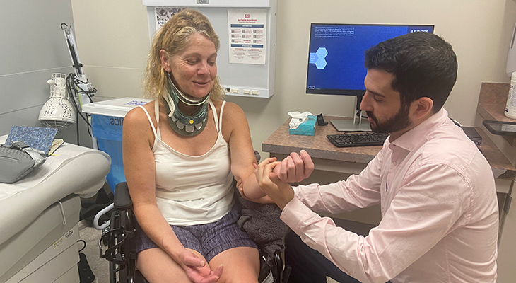 Patti Dailey in a wheelchair, wearing a neck support. Dr. Shane Stone examining the strength in her left hand.