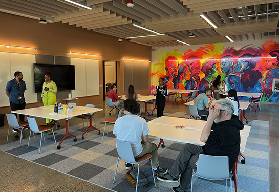 People gather at tables in a modern room with a colorful mural on the wall.