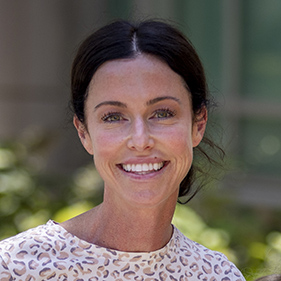 Headshot of woman with brown hair pulled back in a white tshirt with a pattern on it.