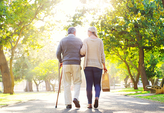  Rearview shot of a young woman assisting her senior father walk at the park