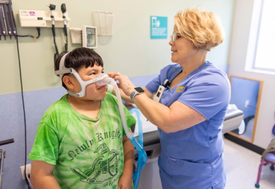 Child with green shirt being fitted with oxygen mask by respiratory therapist. 