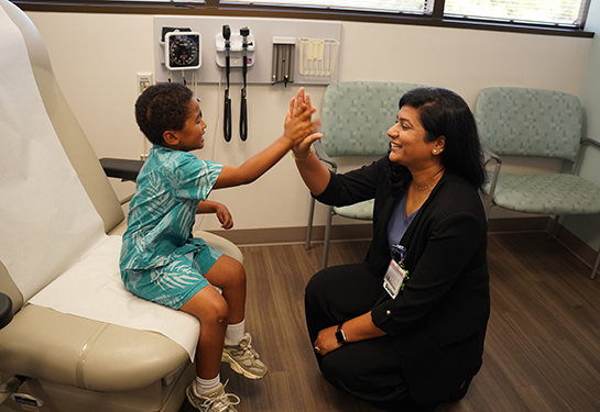 A young boy high-fives his doctor in a neutral-colored exam room. 